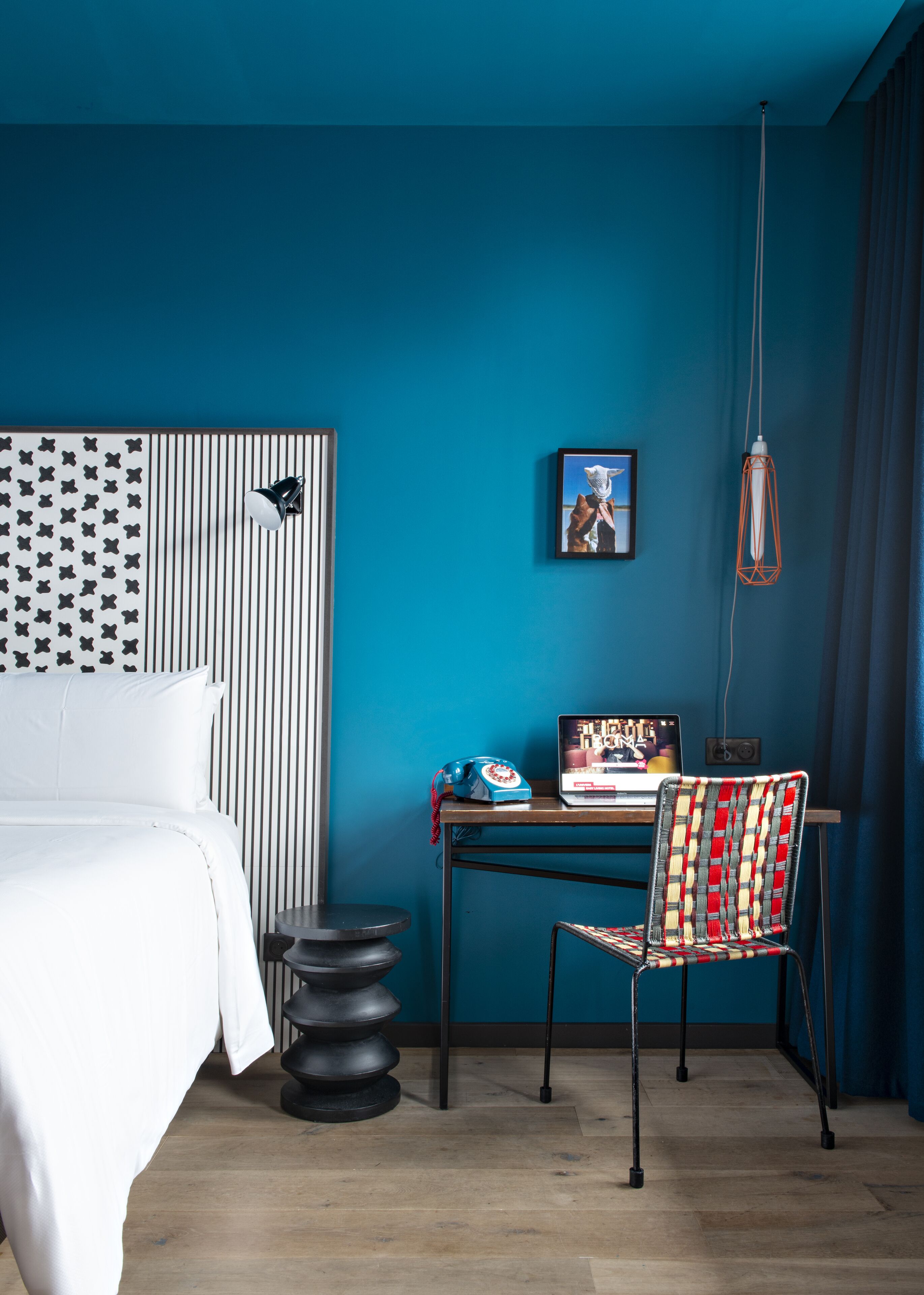 A modern hotel room with a bed, a desk with a laptop, a chair, and a unique wall design.