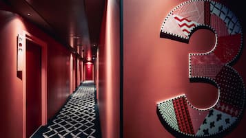 Un pasillo con piso estampado, paredes rojas y un número '3' iluminado de gran tamaño.