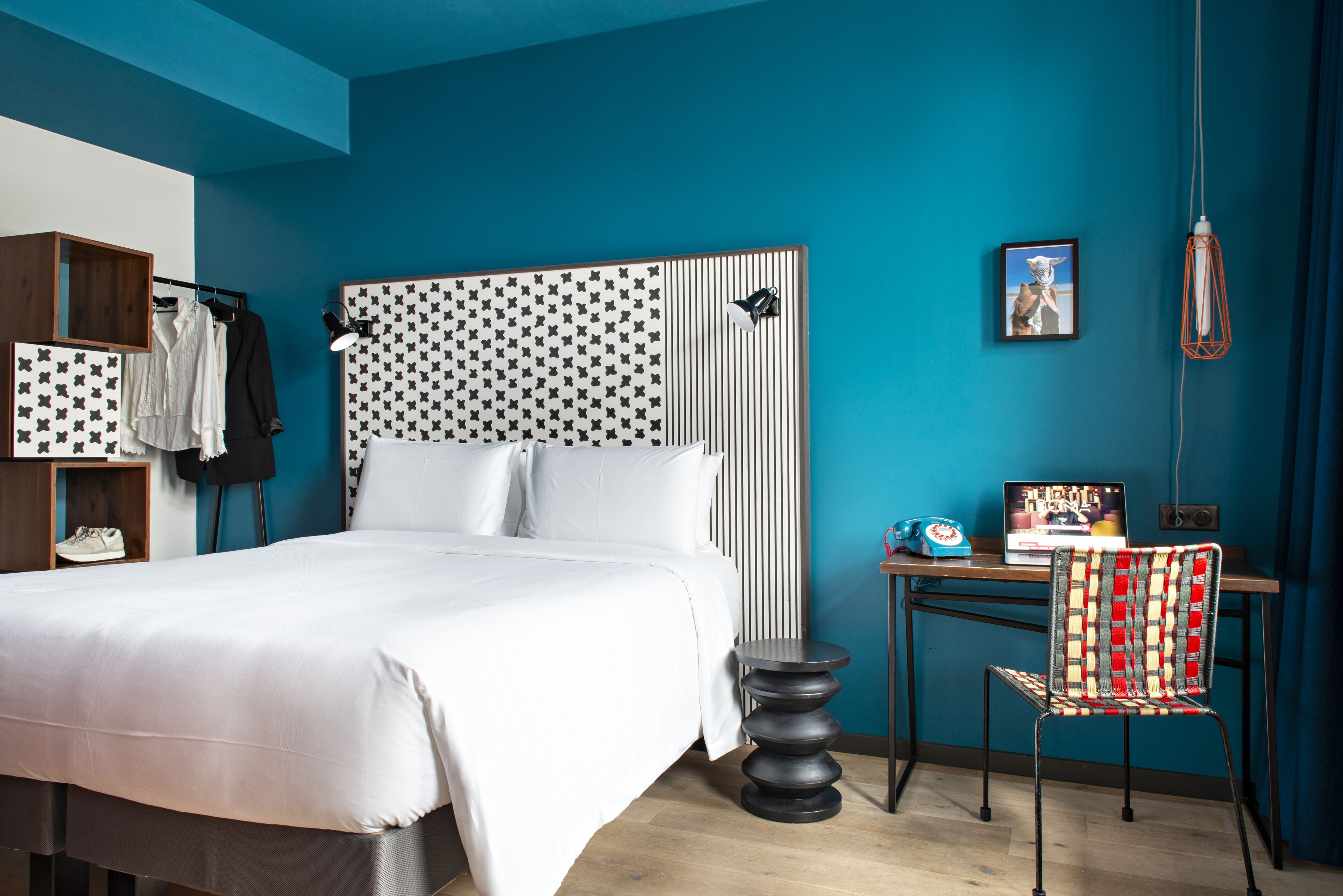 A modern bedroom with a large bed, a desk with a chair, a wardrobe, and a wall-mounted lamp.
