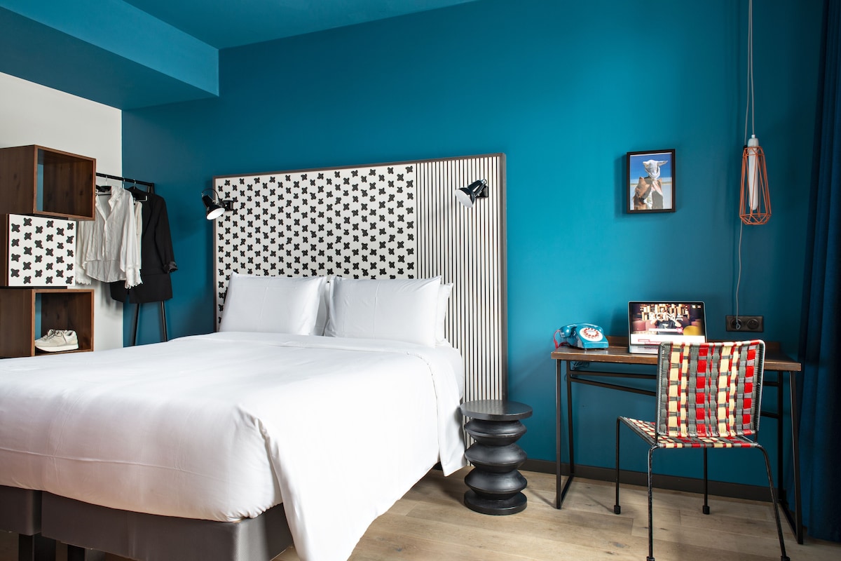 Een moderne slaapkamer met een groot bed, een bureau met stoel, een garderobe en een wandlamp.