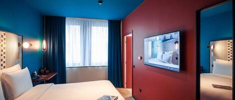 A hotel room with a large bed, a TV mounted on the wall, and a mirror on the opposite wall.