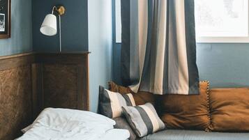 Un dormitorio con cama, un banco, una lámpara y una ventana con cortinas.