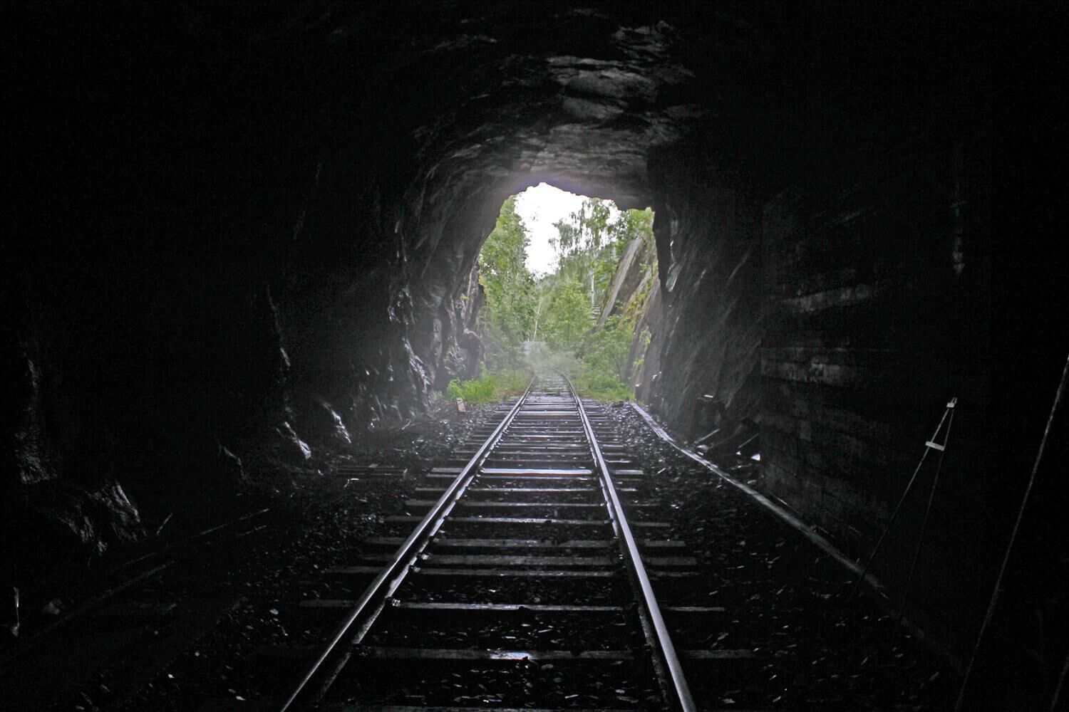 Un tunnel ferroviaire dont les voies mènent à une sortie lumineuse.