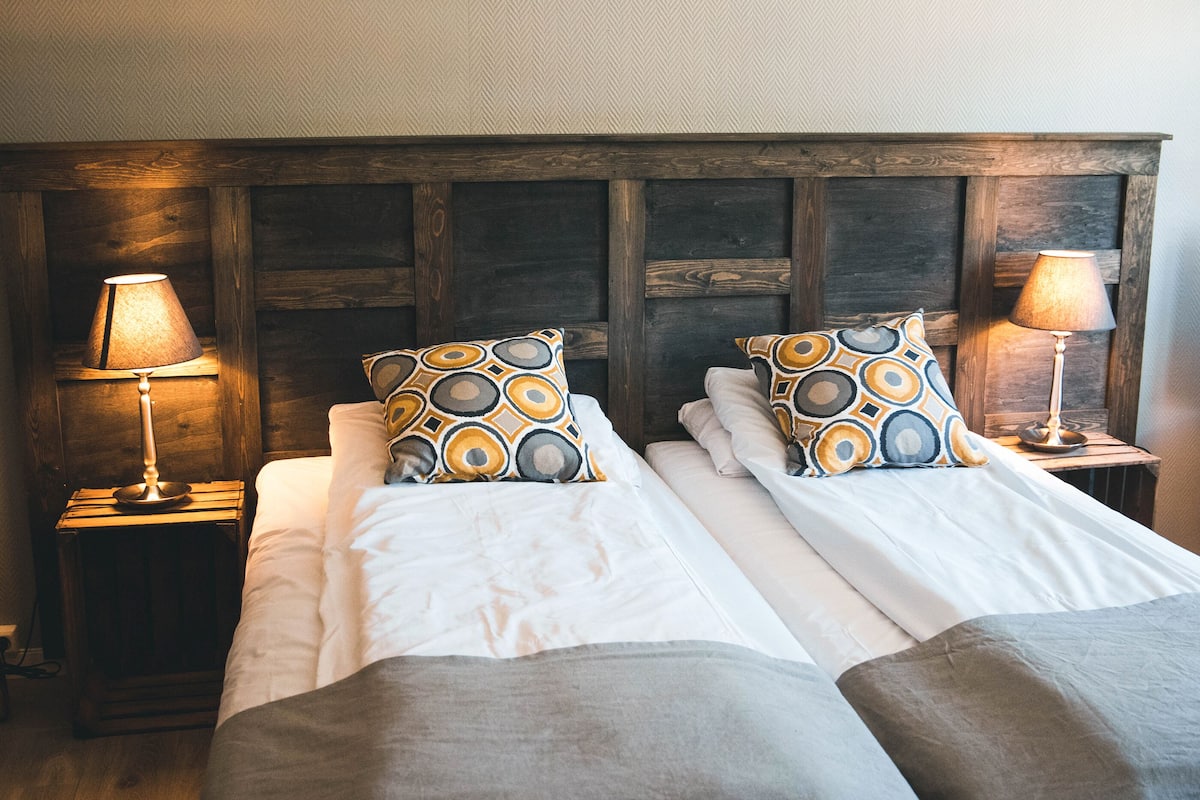 A double bed with two pillows, a wooden headboard, and two bedside lamps.