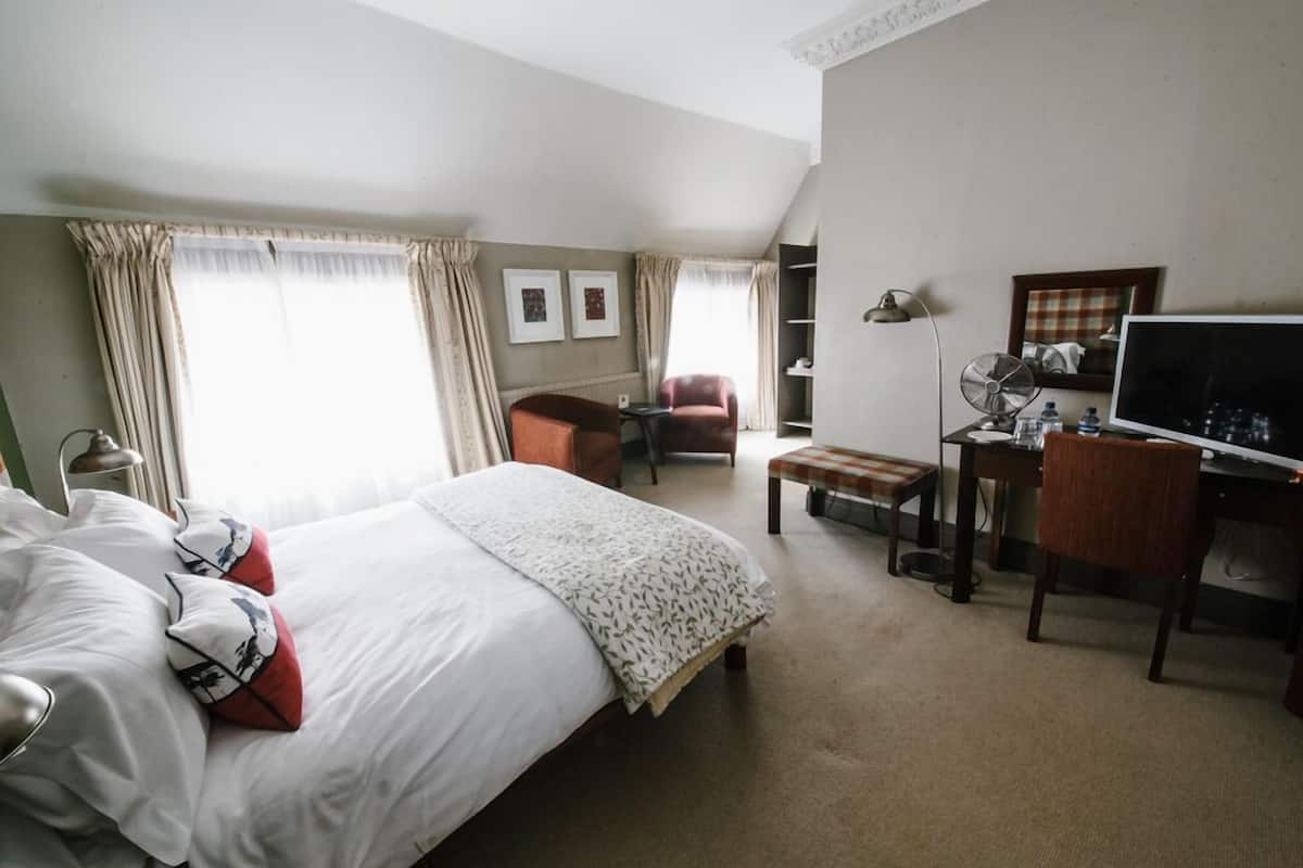 A hotel room with a bed, a desk, a chair, a lamp, and a television.