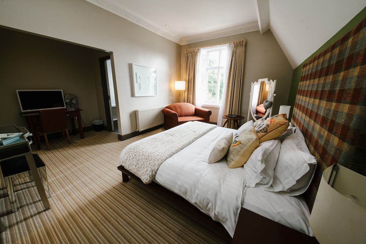 A hotel room with a bed, a desk, a chair, a lamp, and a window with curtains.