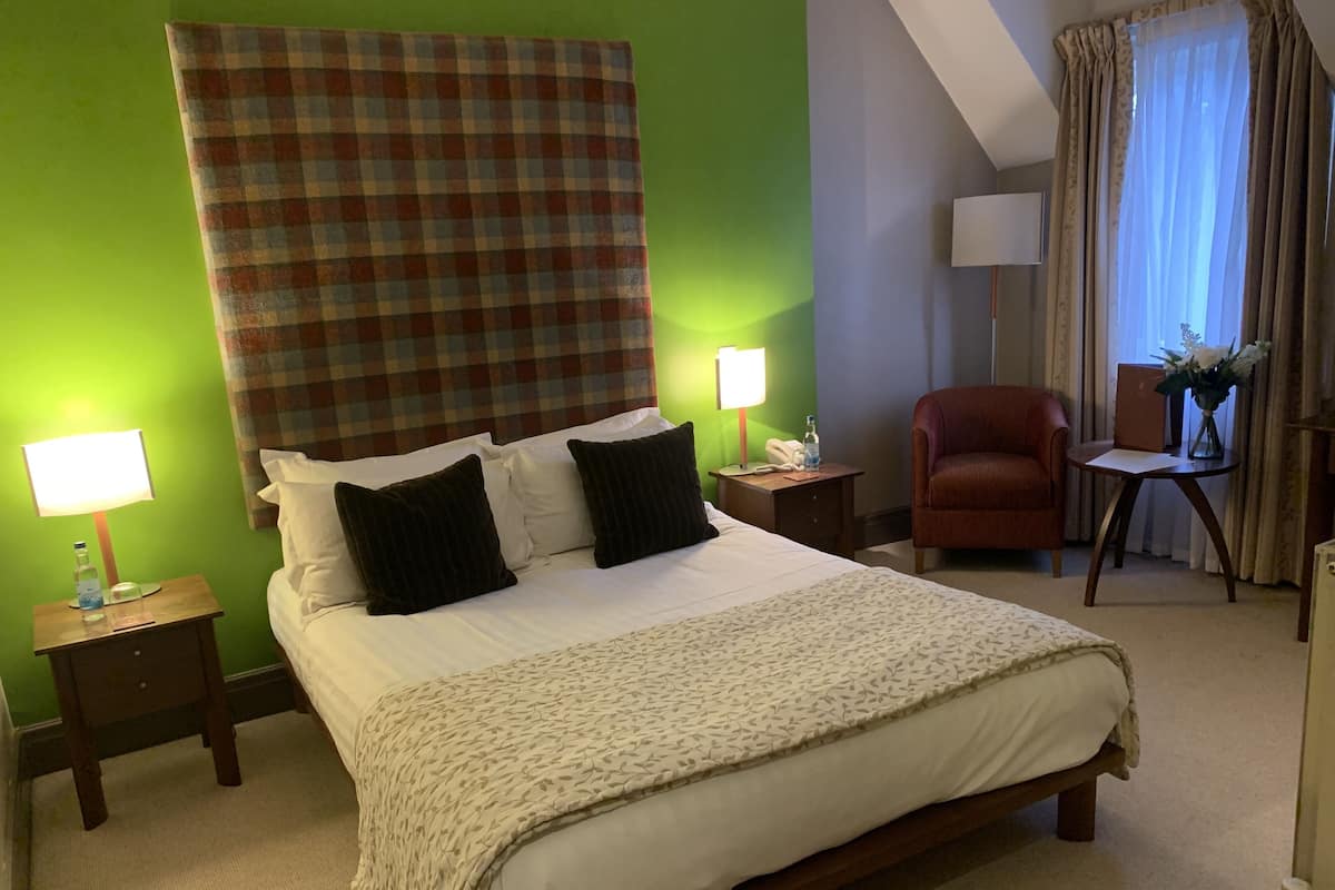 A hotel room with a large bed, two bedside tables, a chair, a desk, and a lamp.
