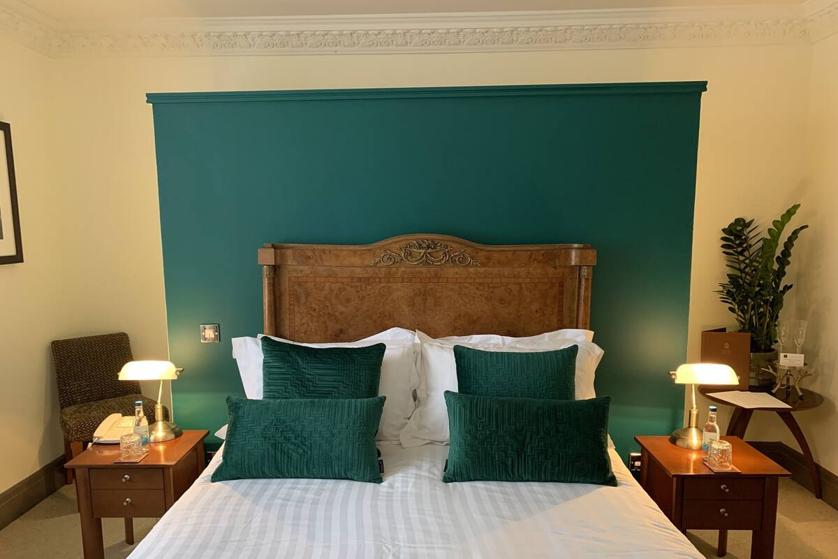 A neatly made bed with a wooden headboard, two bedside tables with lamps, and a green accent wall.