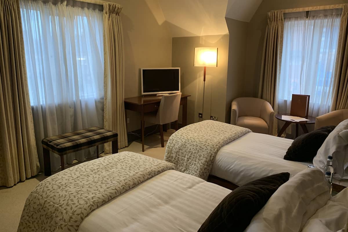 A hotel room with two beds, a desk with a computer, a chair, a small table, and a lamp.
