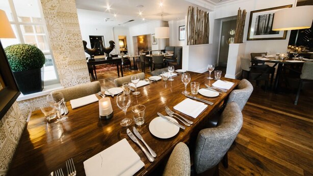 Comedor con una larga mesa de madera dispuesta para seis personas, rodeado de sillas tapizadas.