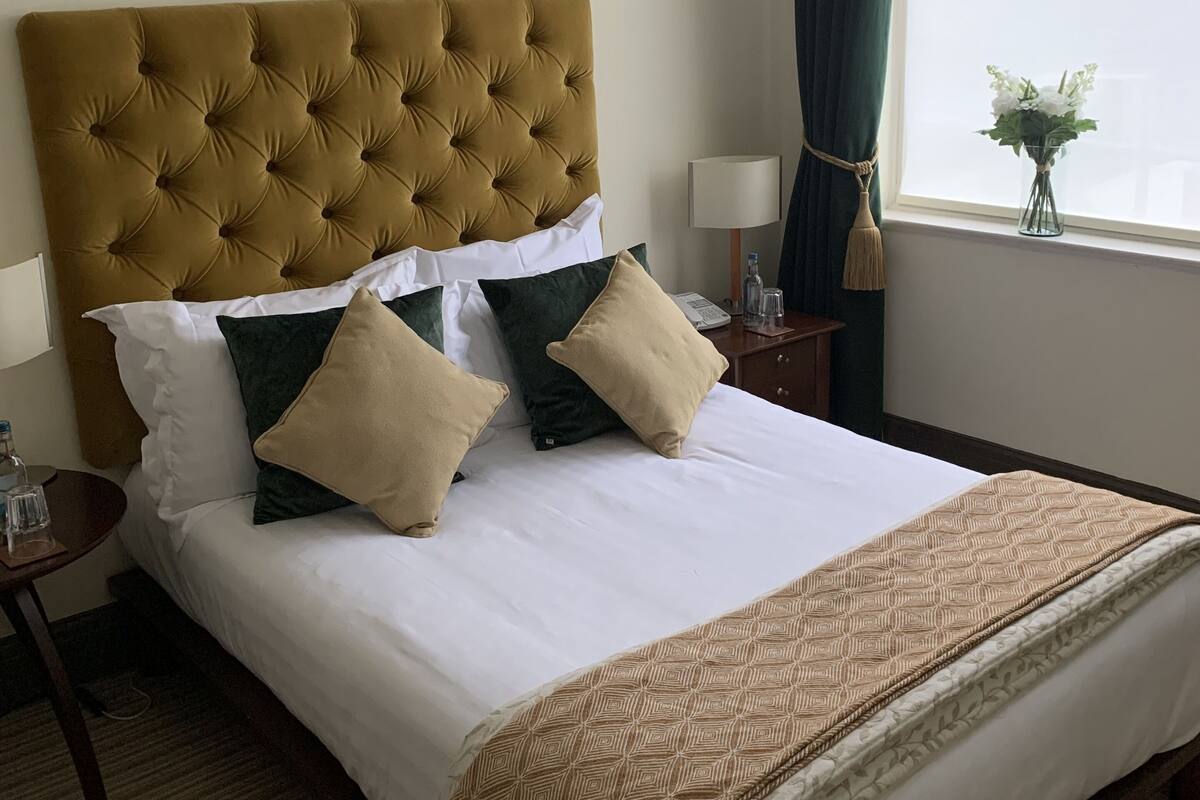 A hotel room with a large bed, a tufted headboard, and a window with a view.