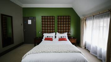 Habitación de hotel con una cama grande, dos mesitas de noche, una pared de acento verde y una ventana con cortinas translúcidas.