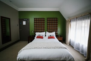 Habitación de hotel con una cama grande, dos mesitas de noche, una pared de acento verde y una ventana con cortinas translúcidas.