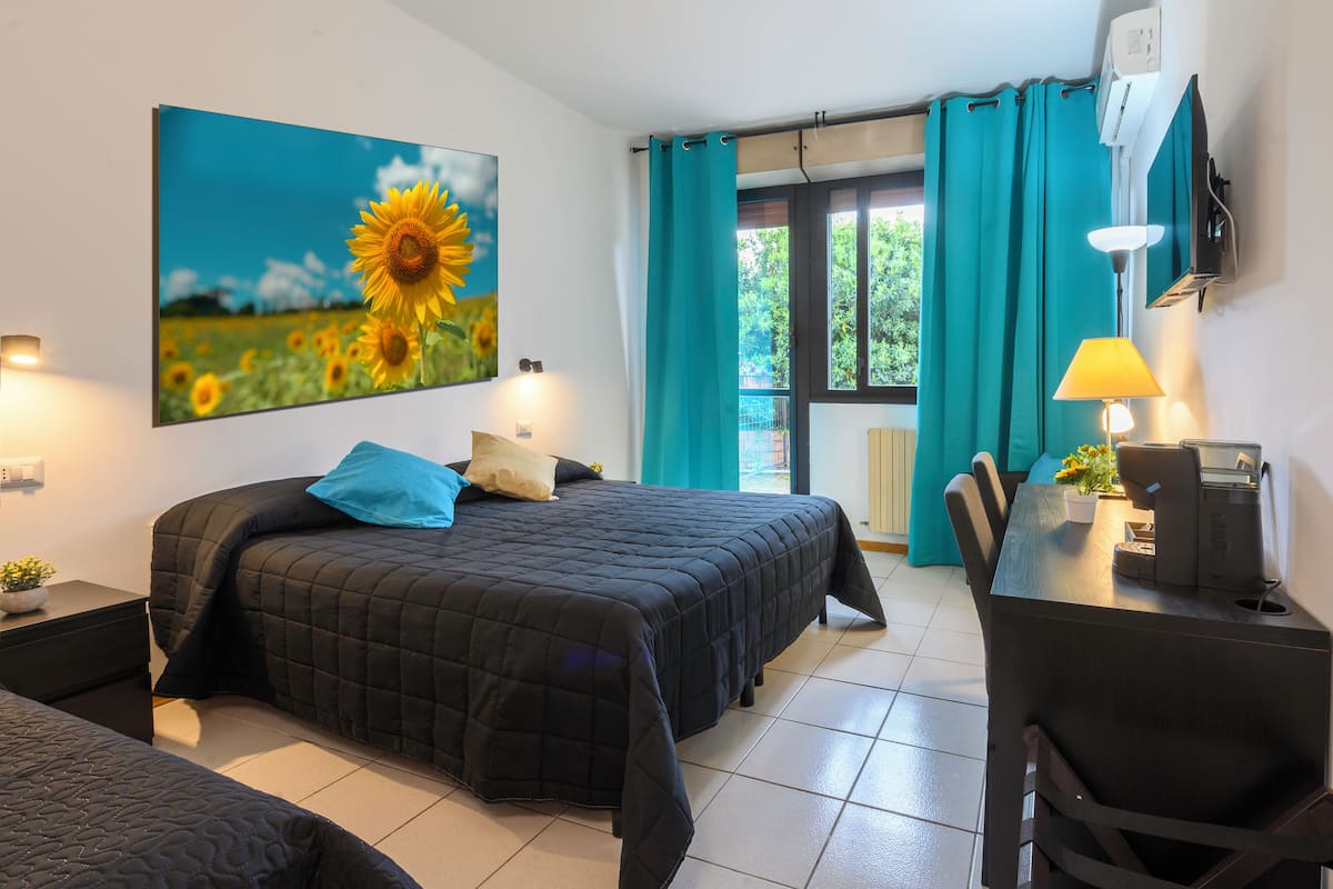Un dormitorio con cama, un escritorio y una silla. Hay una ventana con cortinas y un cuadro de girasoles en la pared.