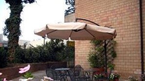 An outdoor patio with a brick wall, a table with chairs, and a large umbrella. - Hotel Anna Siena Nord (Monteriggioni)