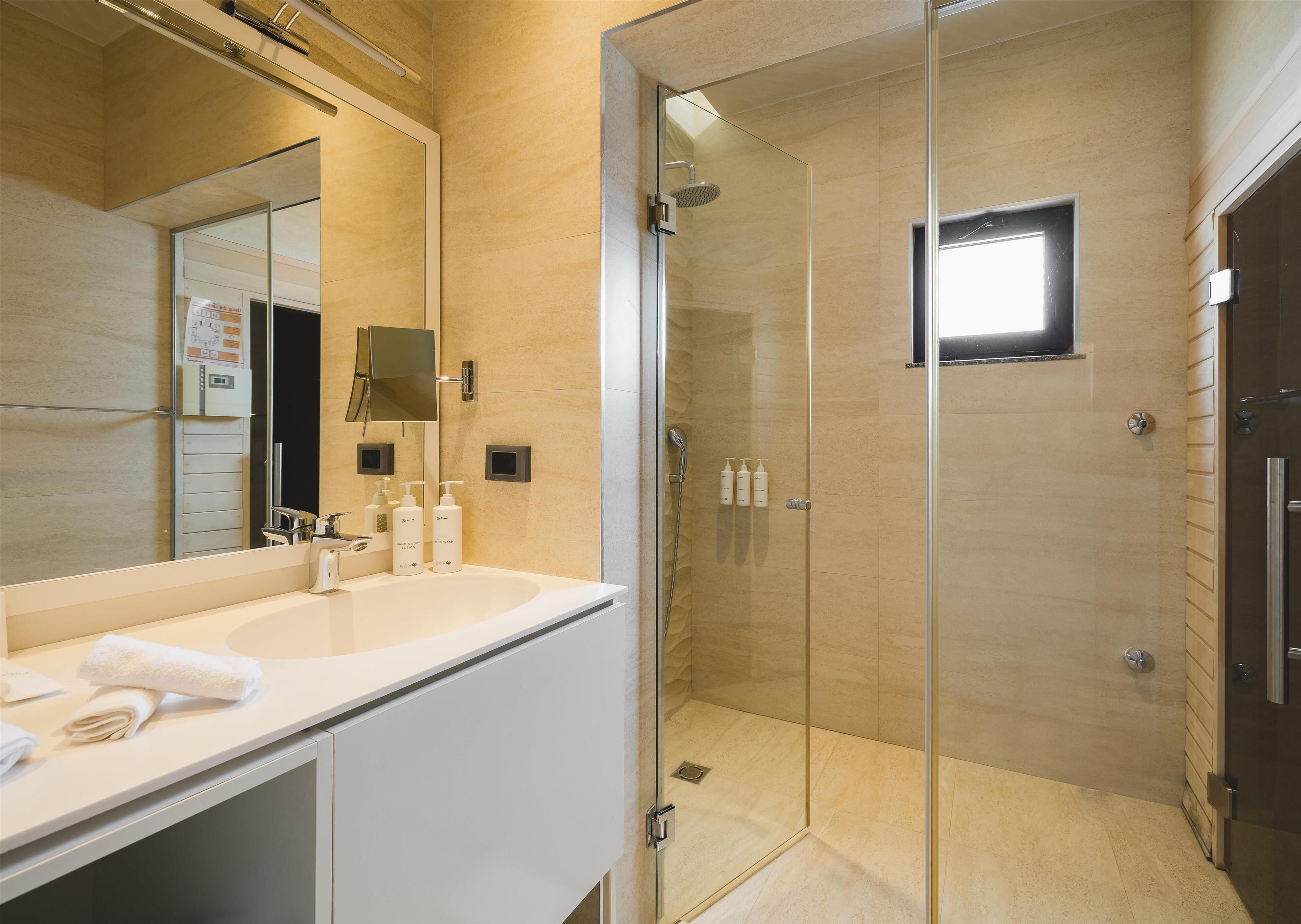 Une salle de bain moderne avec une douche à parois de verre, un grand miroir et un meuble-lavabo blanc.