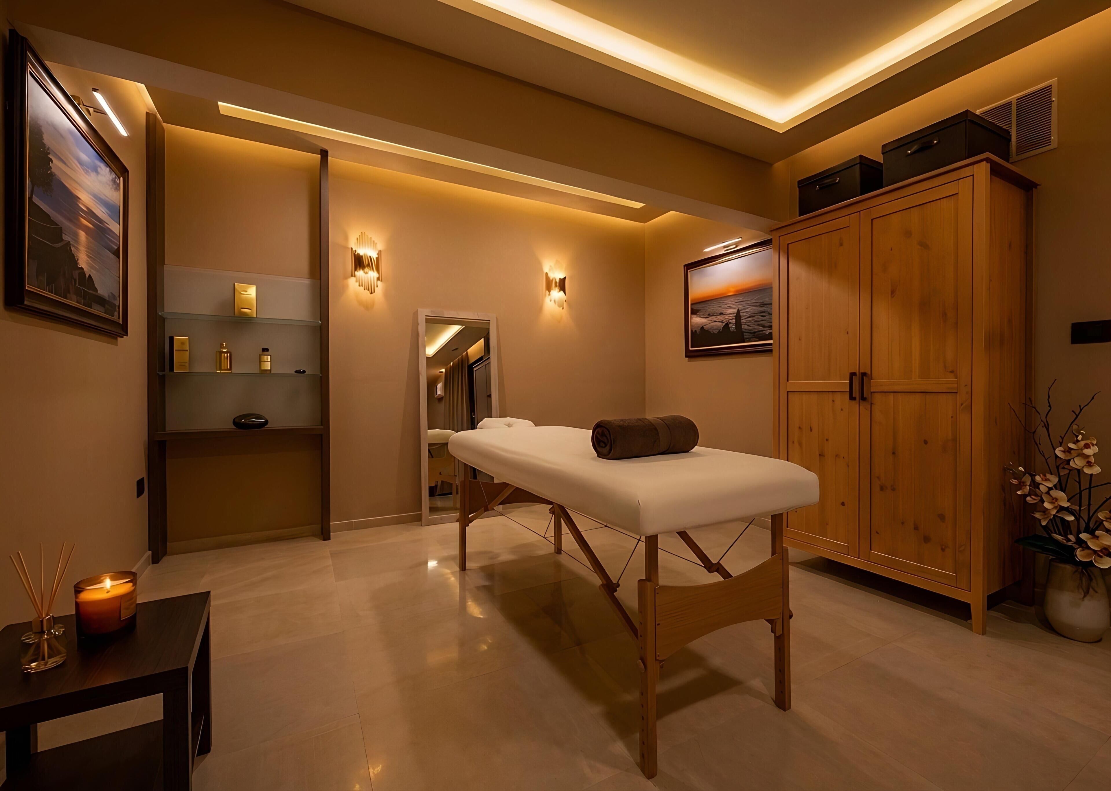 A spa room with a massage table, wooden cabinets, a mirror, shelves with toiletries, and a framed picture on the wall.