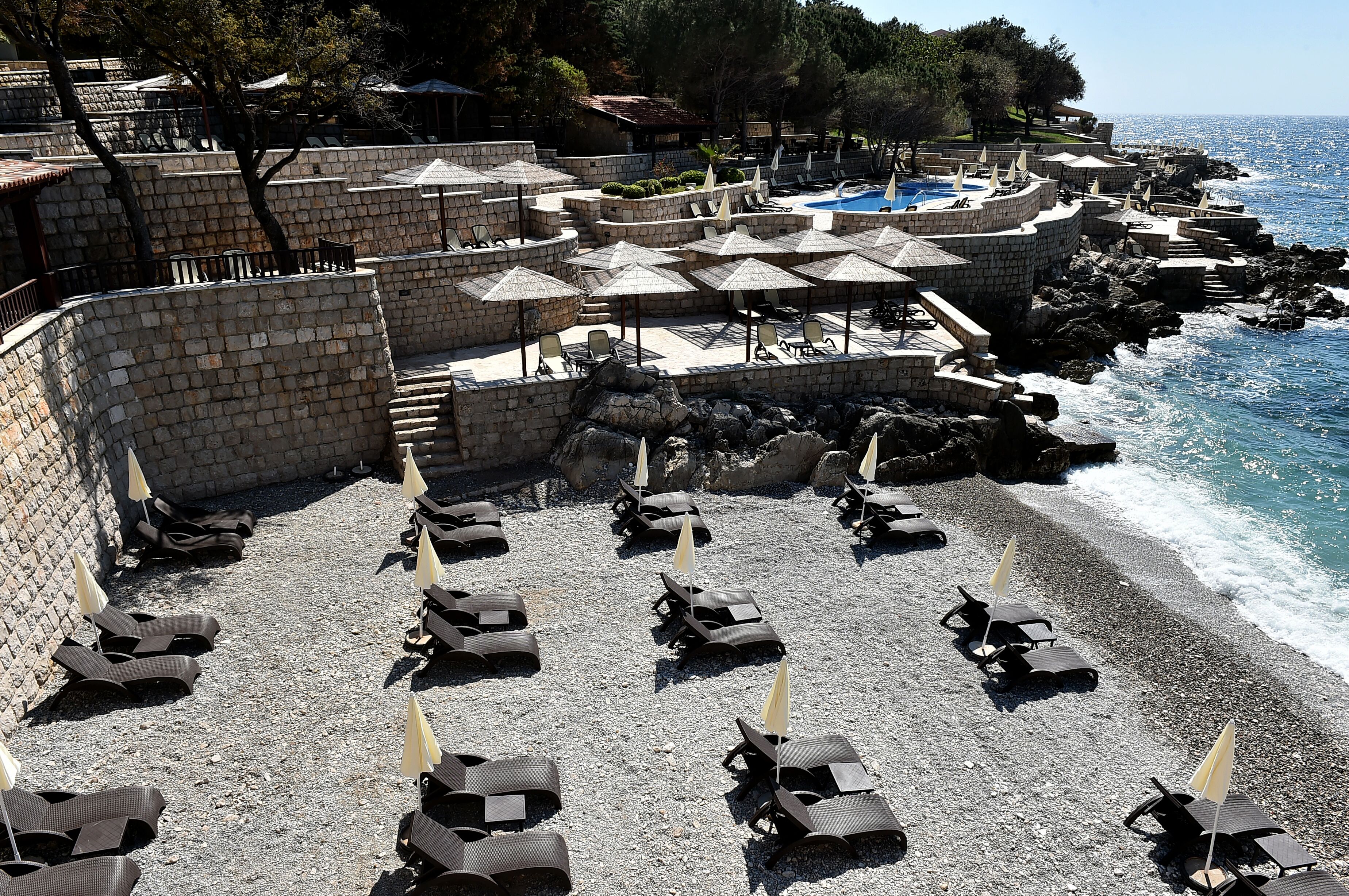 A beachside resort with sun loungers and umbrellas, a pool, and a view of the sea.