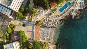 An aerial view of a resort with a pool area, lounge chairs, and a rocky coastline. - Radisson Resort Ruza Vjetrova (Bar)