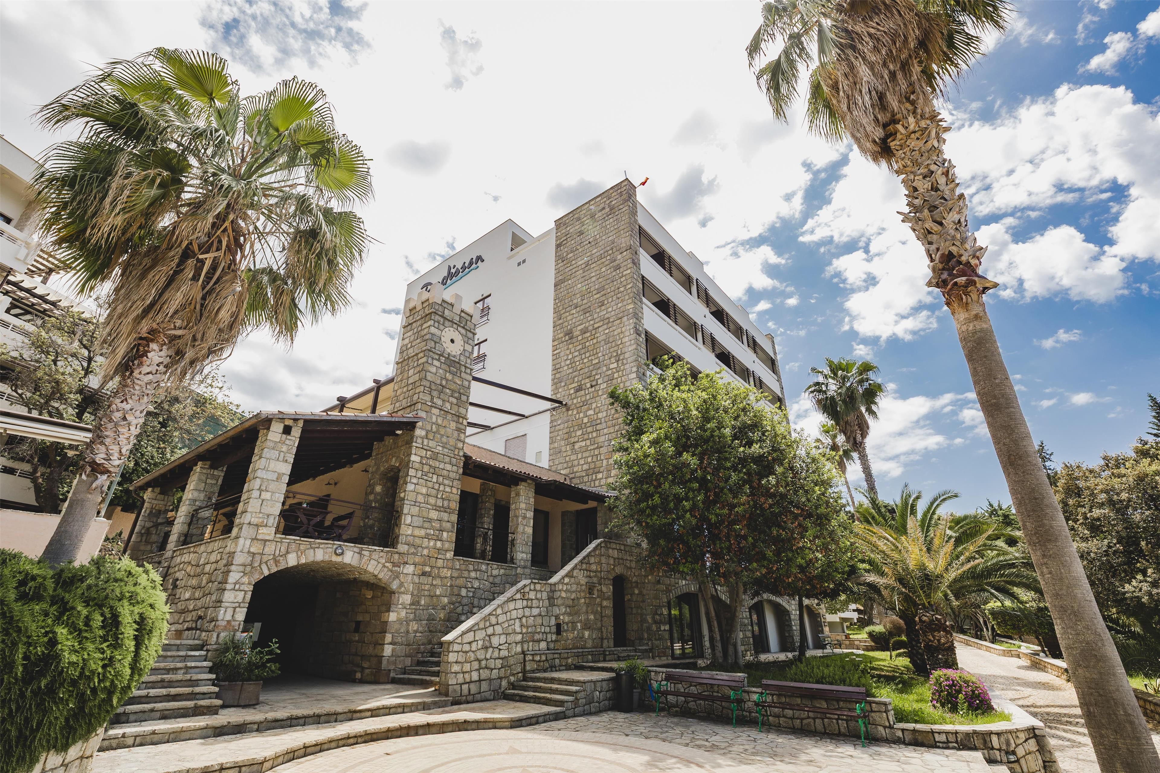 A stone building with a balcony and a palm tree in the foreground.