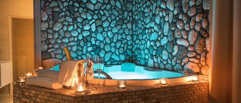 Un área de spa con pared de piedra, un jacuzzi, velas y una botella de champán.