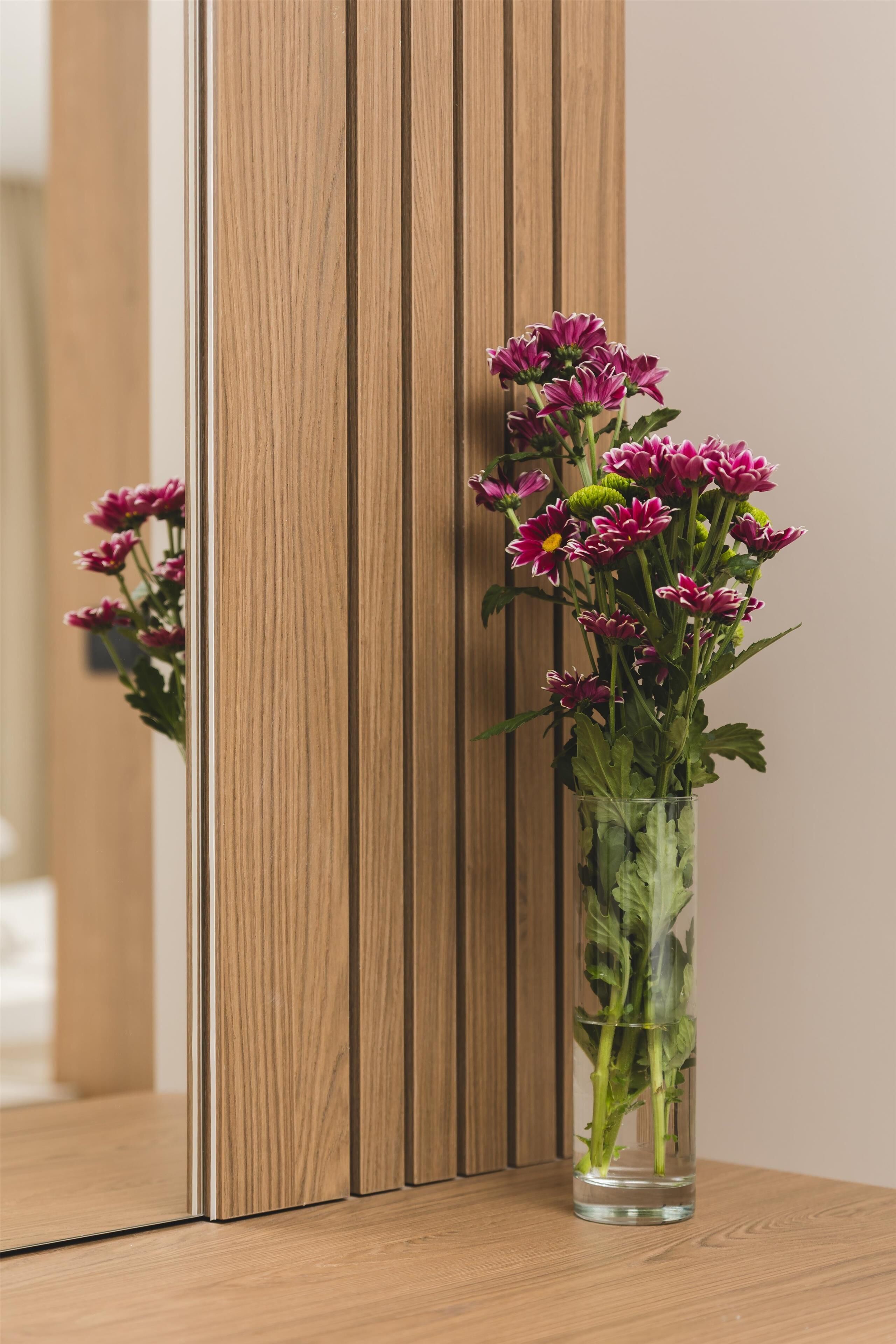 A clear glass vase with pink flowers on a wooden surface.