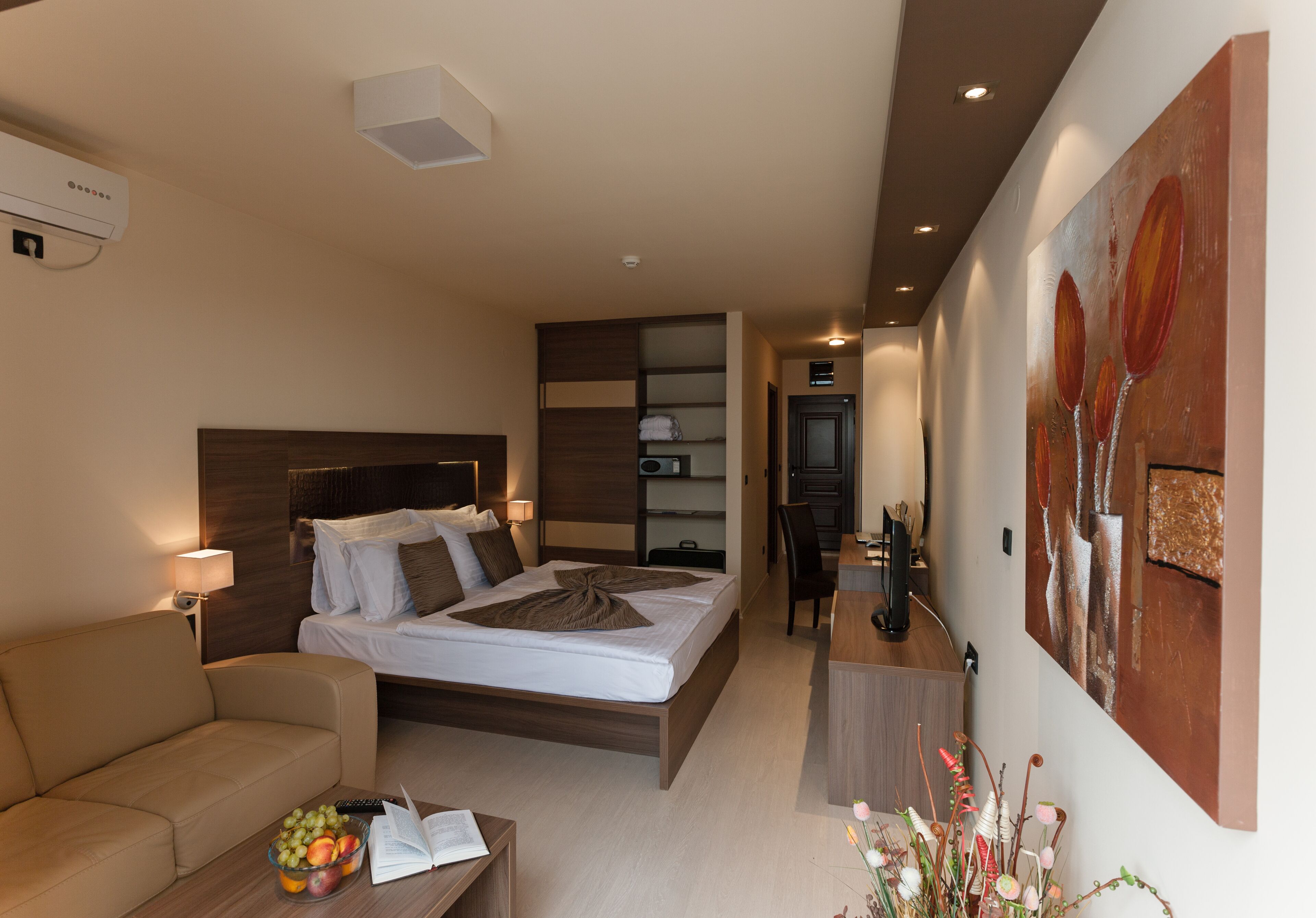 A modern hotel room with a bed, a sofa, a desk, and a large painting on the wall.