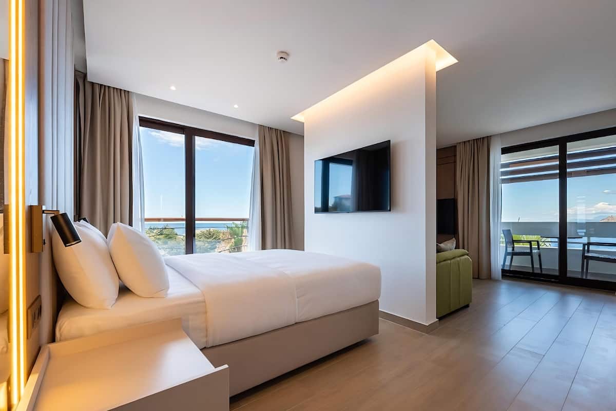 Une chambre d’hôtel moderne dotée d’un grand lit, d’une télévision à écran plat, d’un balcon avec une table et des chaises, et offrant une vue sur le paysage urbain.