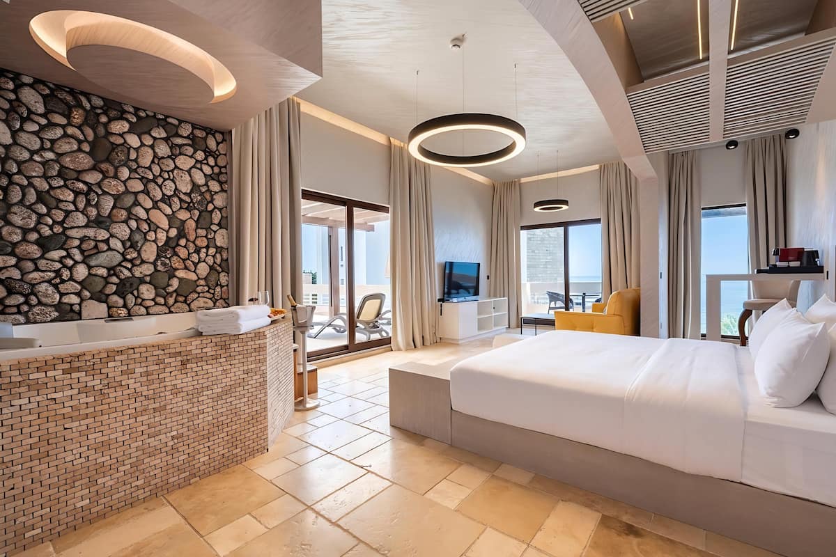 Une chambre d’hôtel moderne avec un mur en pierre, un grand lit, un coin salon avec vue et un balcon.
