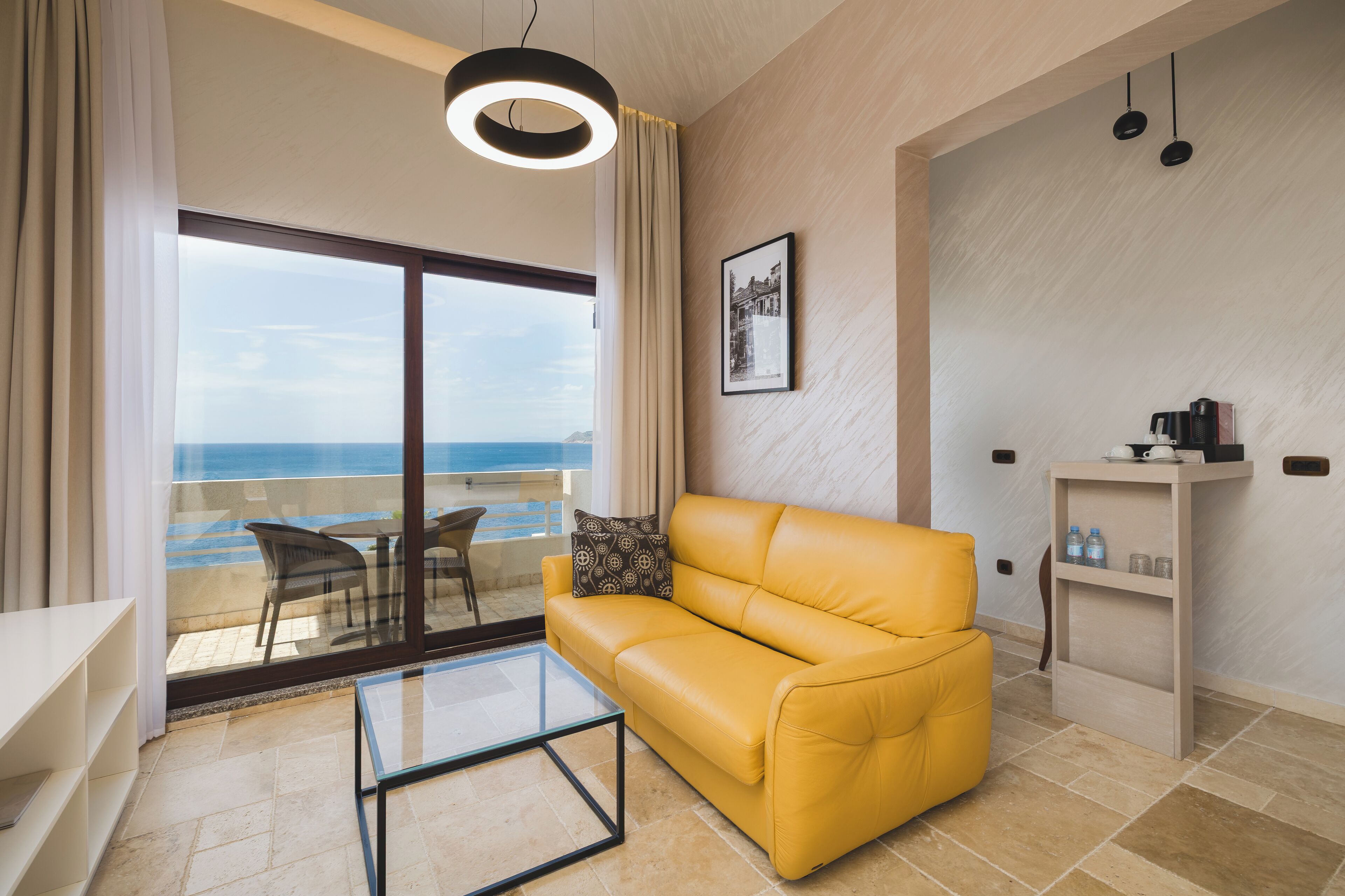 Una sala de estar moderna con un sofá amarillo, una mesa de centro de vidrio y vista al mar a través de un ventanal grande.