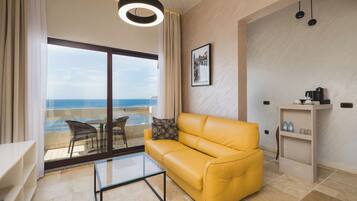 Una sala de estar moderna con un sofá amarillo, una mesa de centro de vidrio y vista al mar a través de un ventanal grande.