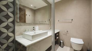 Un baño moderno con un espejo grande, un lavamanos blanco, un inodoro y una zona de ducha con mampara de vidrio.