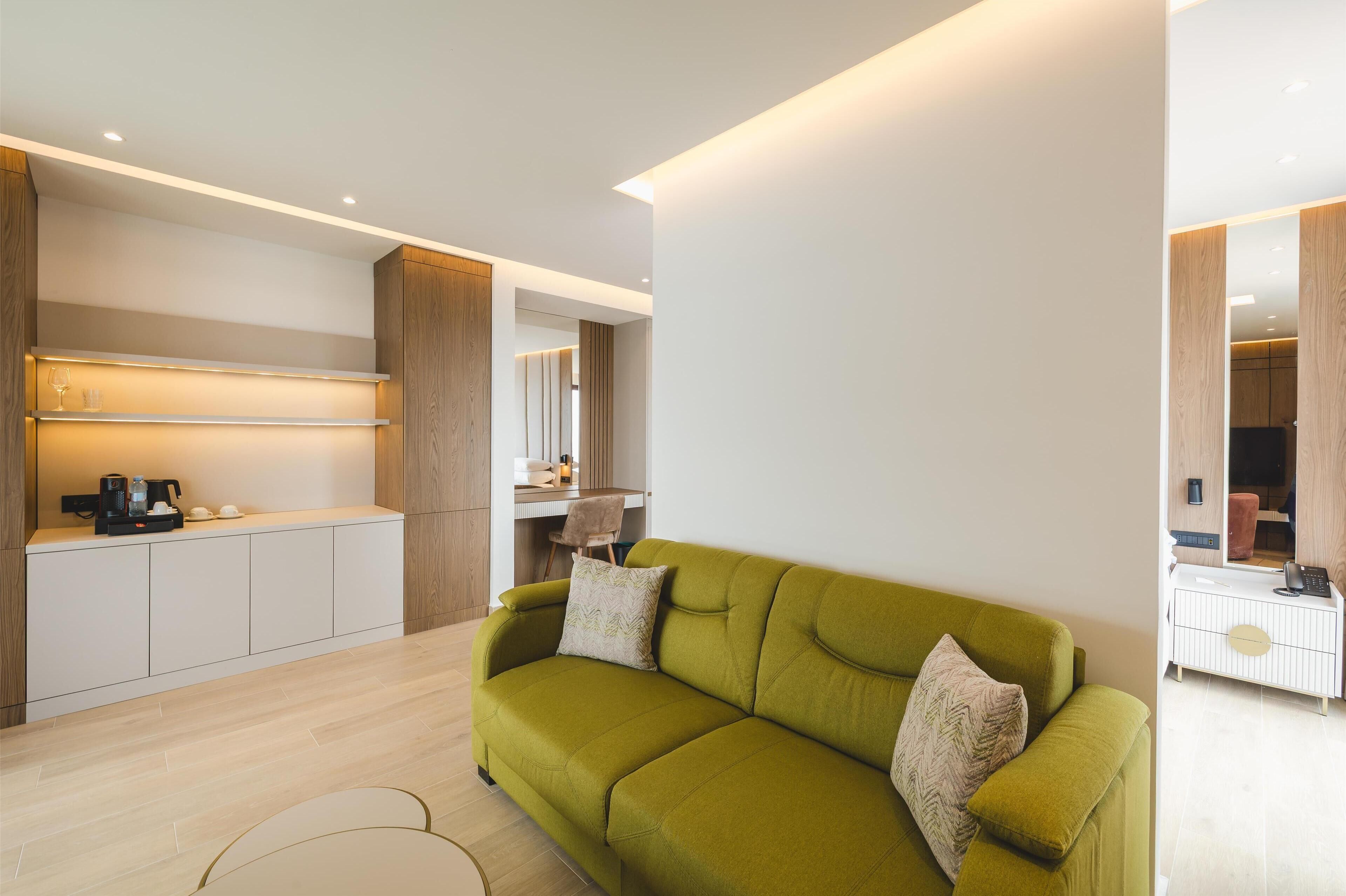 Un salón moderno con un sofá verde, una zona de cocina con encimera y un armario con espejo.
