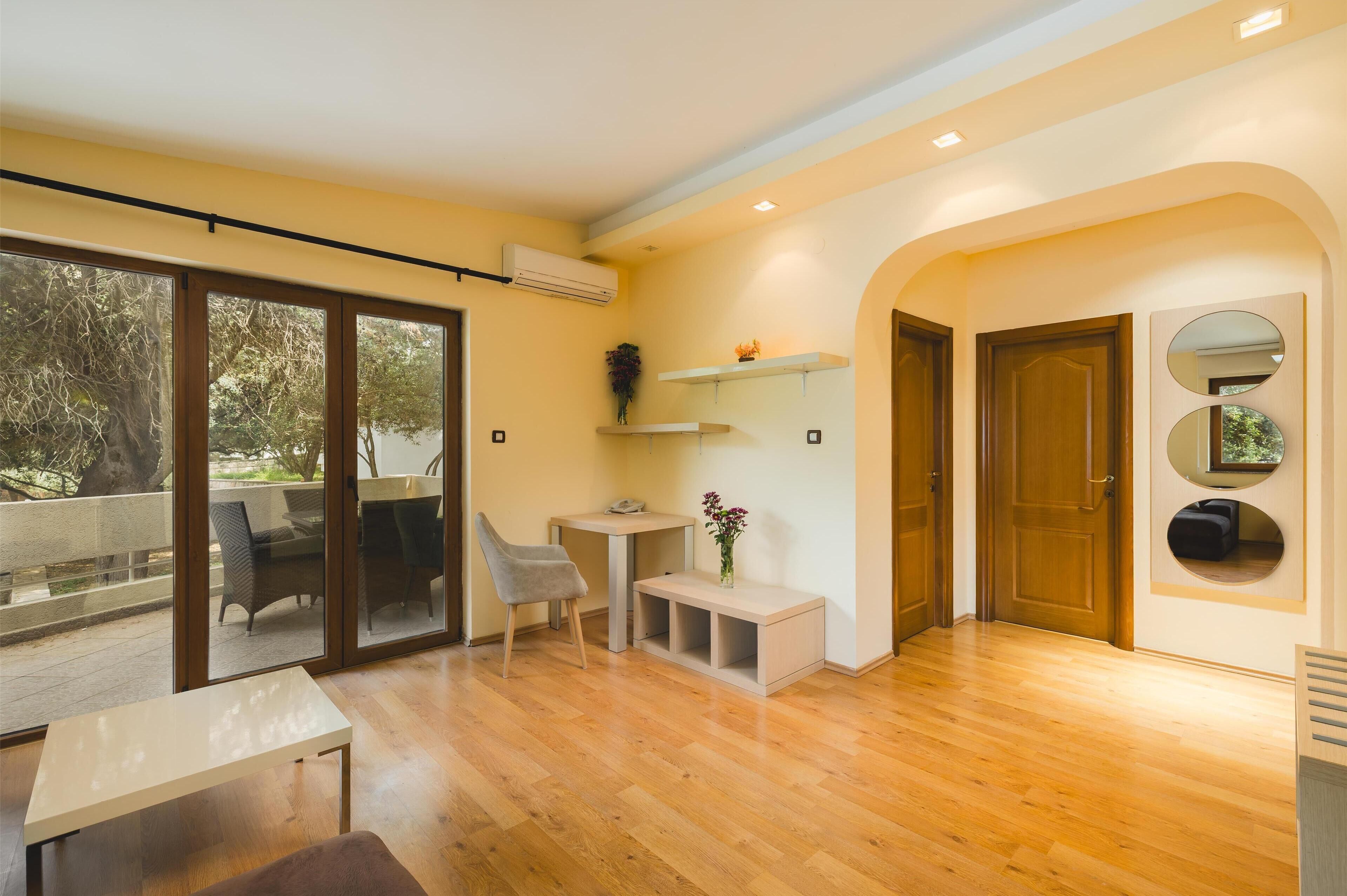 Un interior moderno con piso de madera, un ventanal corredero que da a un balcón, una pequeña mesa, una silla y un banco.