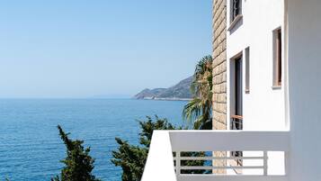 A white building with a balcony overlooking a clear blue sea and distant mountains.