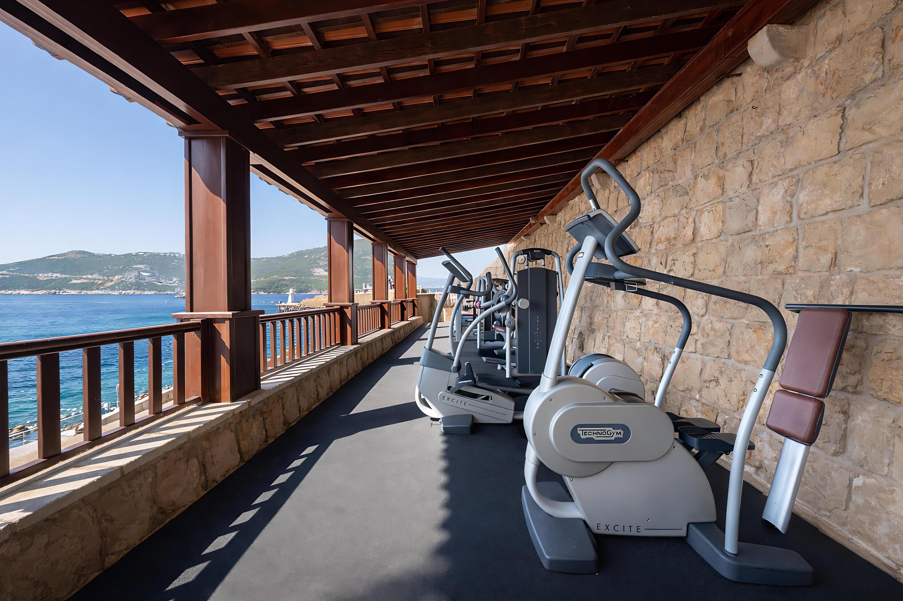 An outdoor gym area with exercise equipment, a stone wall, and a view of the sea.