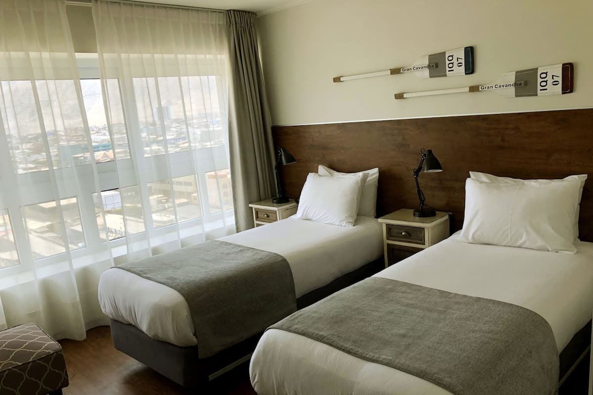 Habitación de hotel con dos camas, vista a la ciudad y cabecero de madera.