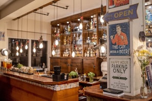 Un bar avec un comptoir, des lampes suspendues et un panneau indiquant les places de stationnement réservées à l’heure de l’apéritif.