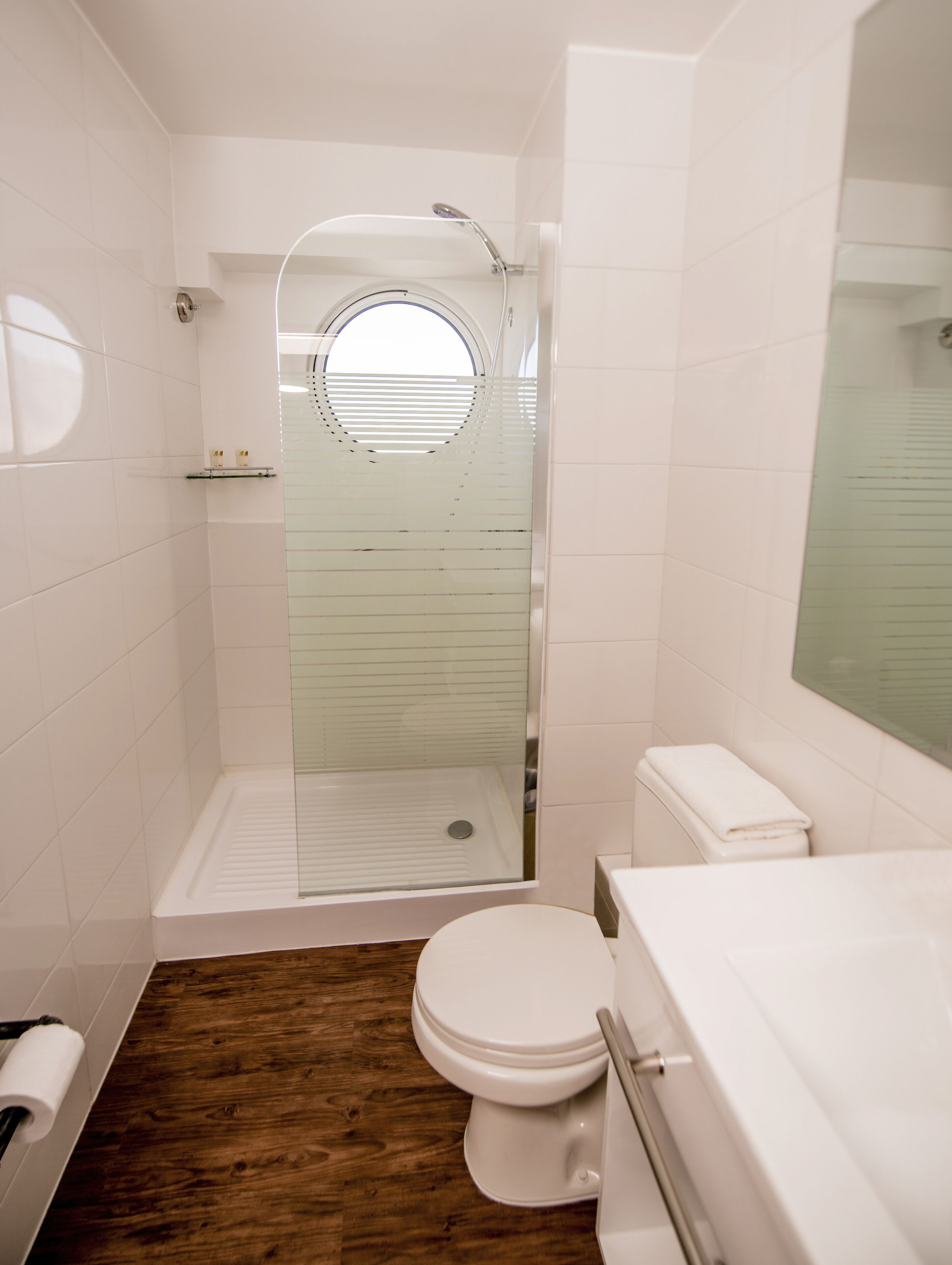 A modern bathroom with a glass-enclosed shower, a toilet, and a wooden floor.
