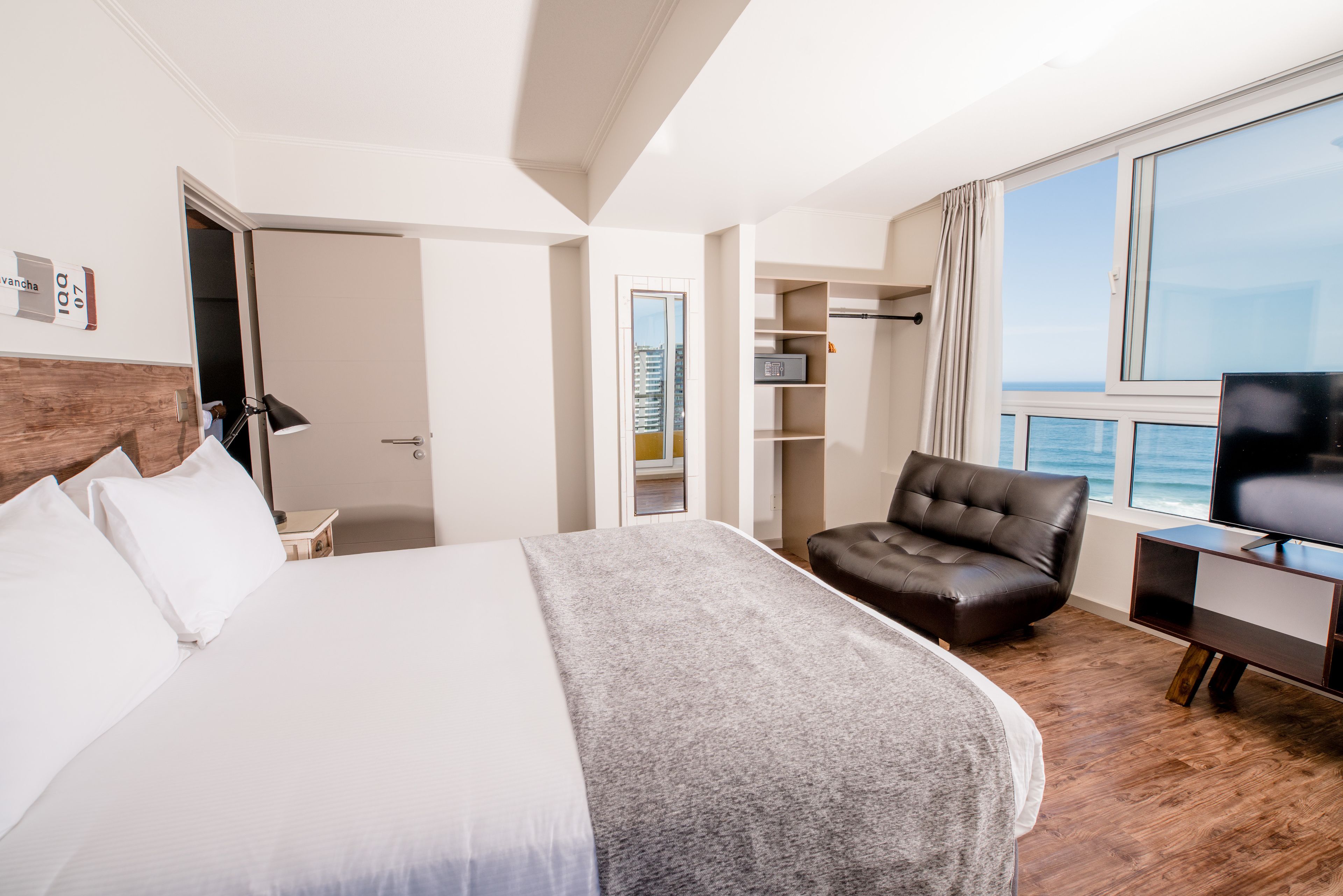 Une chambre d’hôtel avec un grand lit, un fauteuil en cuir, une télévision et une vue sur l’océan.