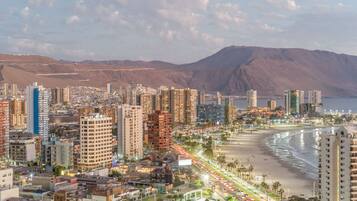Un paisaje costero con rascacielos, una playa y montañas al fondo.