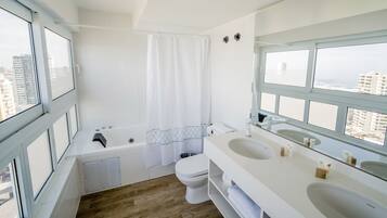 Un baño moderno con bañera, inodoro y ventanas amplias con vistas a la ciudad.