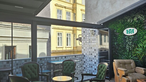 A modern interior with a high ceiling, a green wall with a logo, and a view of a yellow building. - Hotel Devman (Istanbul)
