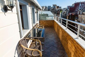 Een balkon met rieten stoelen en een glazen tafel, met uitzicht op een stadsbeeld.