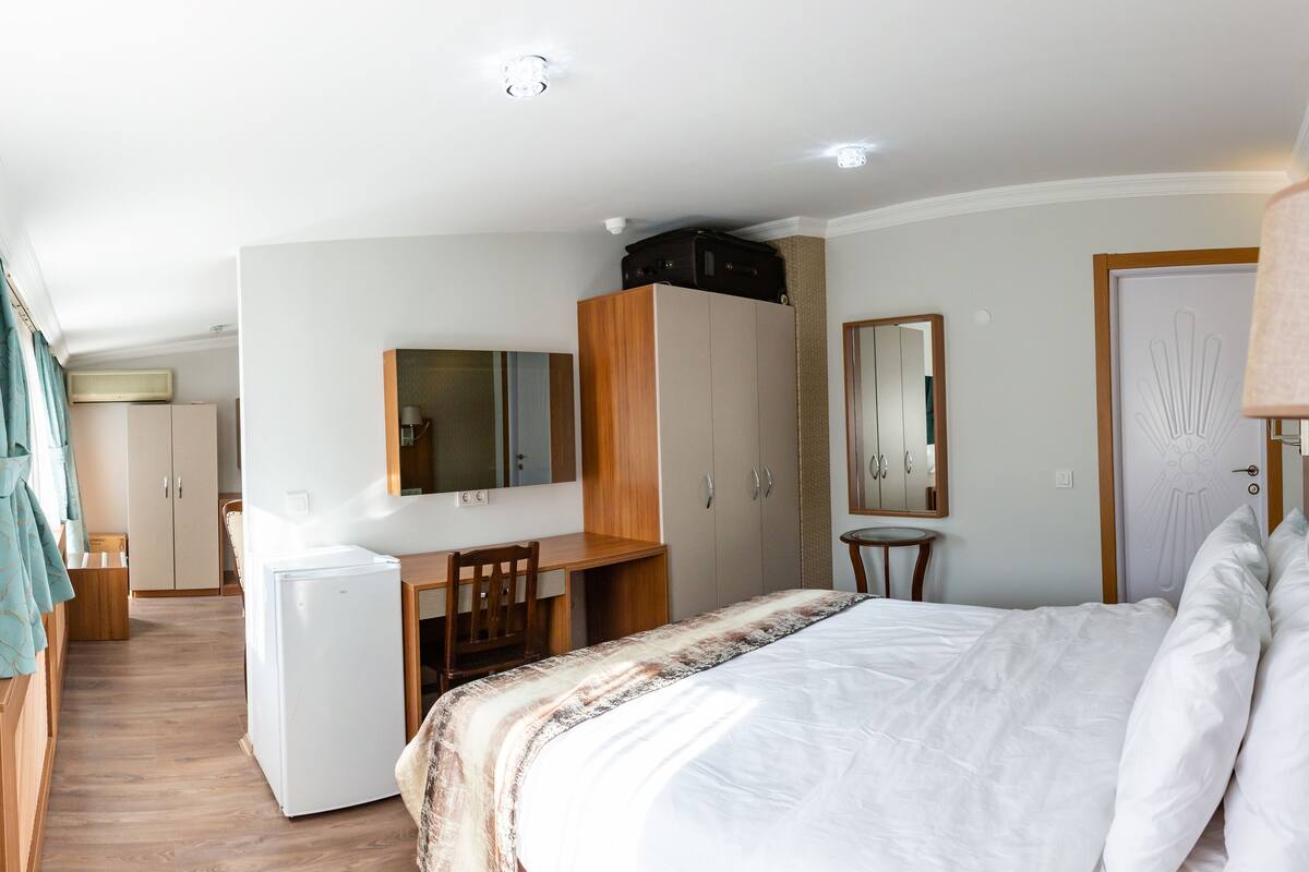 A hotel room with a bed, desk, wardrobe, and a small refrigerator.