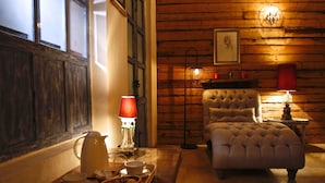 Una habitación acogedora con pared de madera, un sillón capitoné, una mesita de noche con lámpara y una bandeja con tetera y tazas.