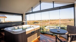 Een hottub op een houten terras met uitzicht op een wijngaard en een landschap in de verte.