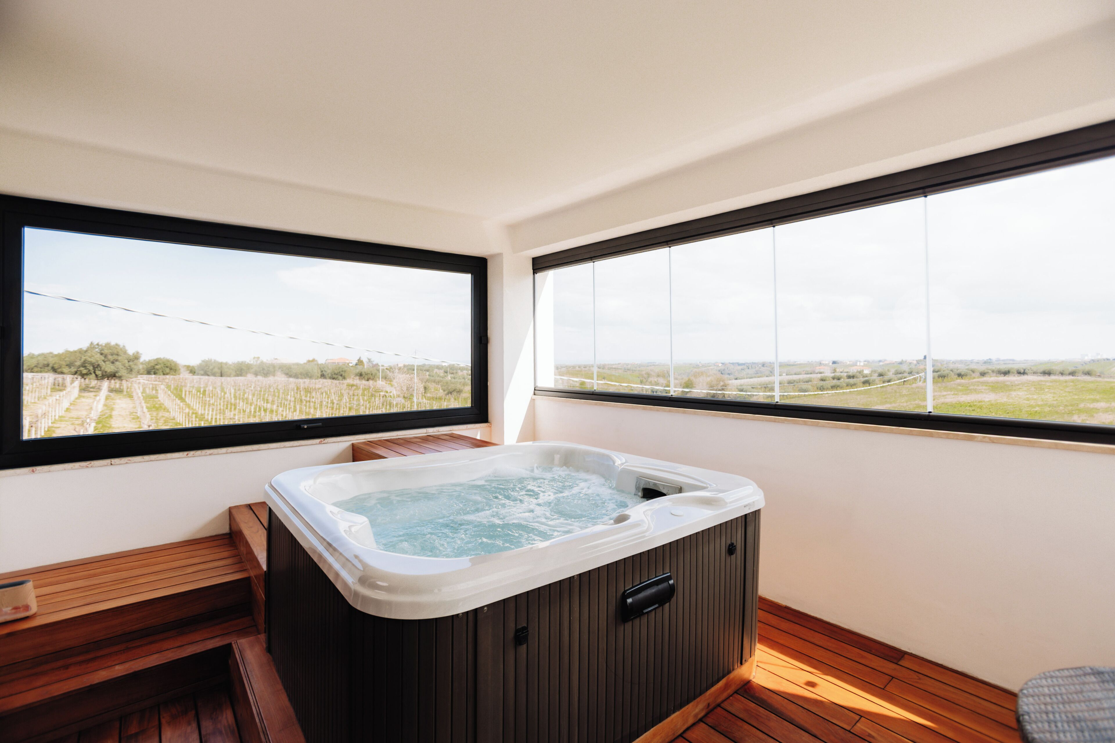 A hot tub in a room with large windows and wooden flooring.