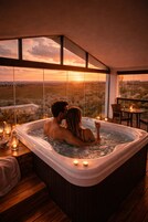 Una pareja en un jacuzzi con vista al atardecer, suelo de madera y velas.