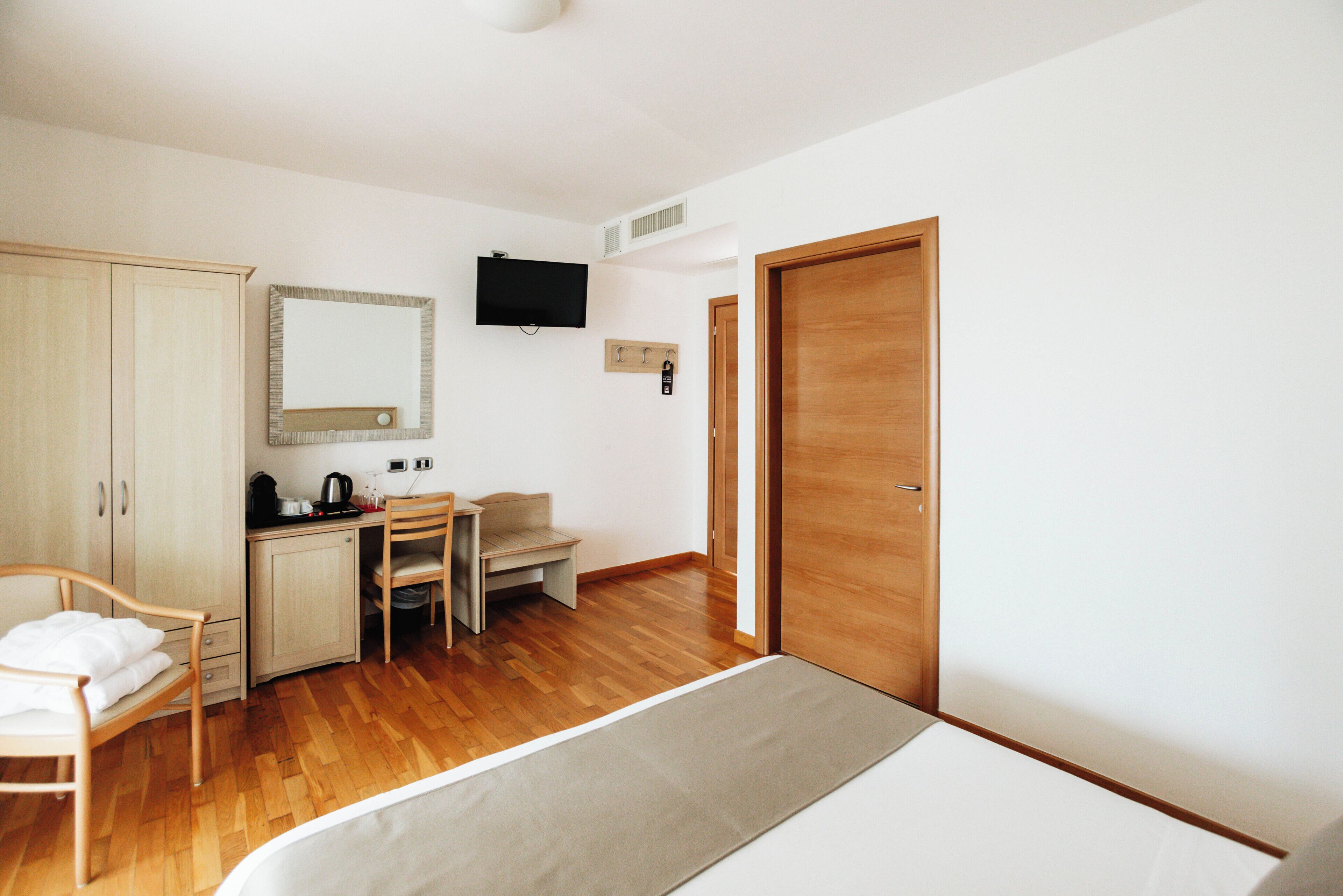 A hotel room with a bed, a desk, a chair, a wardrobe, a television, and a door.